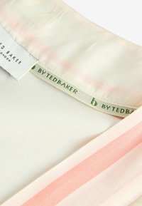 Puuvillapusero, jossa on vaalean kermanvärinen tausta ja vaaleanpunaiset raidat. Kauluksessa on vihreä "By Ted Baker" kudottu etiketti. Sileä rakenne.