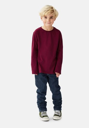 Viininpunainen pitkähiha paita yhdistettynä sinisiin farkkuihin ja vihreisiin korkokenkäisiin tennareihin. Paidassa on pyöreä kaula-aukko ja se on valmistettu pehmeästä kankaasta.