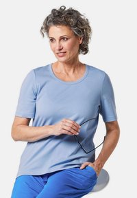 Lichtblauw T-shirt met korte mouwen en een ronde hals, gemaakt van zachte stof, gecombineerd met blauwe broek; model houdt een bril in haar hand.