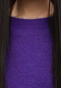 Close-up of a person wearing a purple knitted sweater with long, straight dark hair visible on both sides.