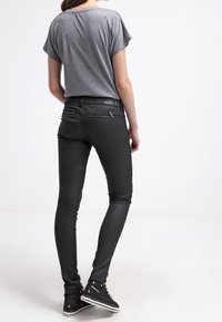 Šedý krátký rukáv top spárovaný s přiléhavými černými kalhotami připomínajícími kůži a černými vysoce střihovými teniskami. Hladká textura s detaily zipu na kalhotách.