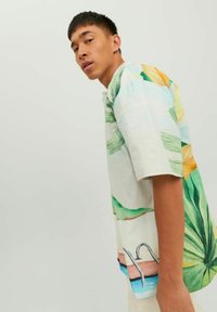 Camicetta a maniche corte realizzata in un tessuto leggero, con grafiche di foglie tropicali e piscine in verde, giallo e blu, dal taglio morbido e leggermente over-size.