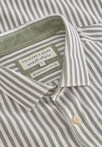 Camicia a righe verde e bianca, con colletto button-down, tessuto testurizzato e etichetta con "Colours & Sons" e taglia L.