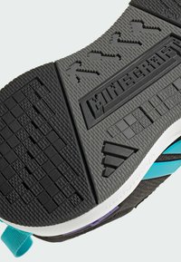 Černá gumová podrážka s texturovanými vzory, vybavená modrými akcenty a prvky loga; navržena pro trakci a odolnost.