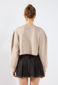 Felpa beige corta con maniche lunghe, abbinata a una gonna plissettata in denim nero con orlo sfilacciato e cuciture dorate.