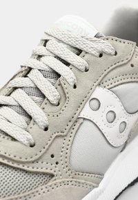 Light gray sneaker with suede and mesh material, featuring white accents, textured laces, and a distinctive logo on the side.