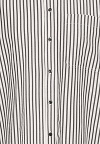 Krekls ar vertikālām melnām un baltām svītrām, ar mazu krūšu kabatu un melnām pogām priekšpusē. Viegls audums.