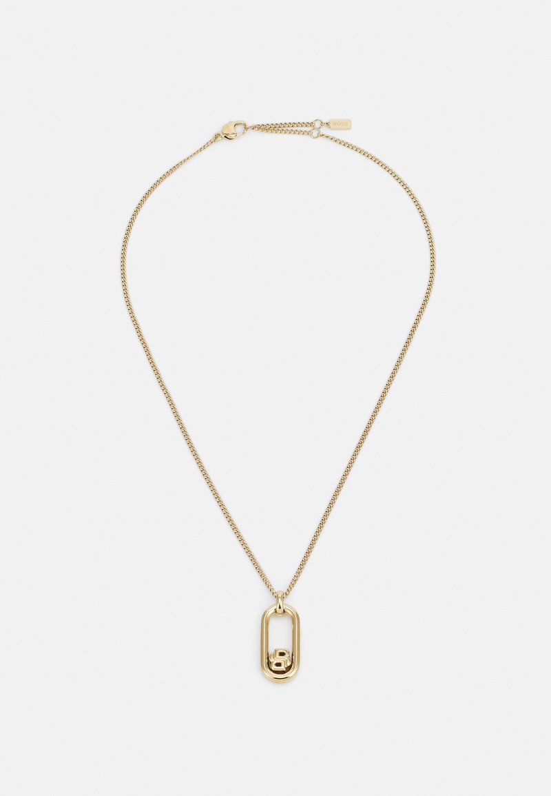 Collier en or avec une chaîne et un pendentif en forme de épingle à nourrice avec un petit détail en forme de lettre "B" à l'intérieur. Texture métallique lisse.