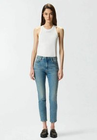 Haut blanc sans manches, coupe ajustée ; jean skinny bleu clair avec texture délavée ; chaussures noires à enfiler avec accents cloutés.