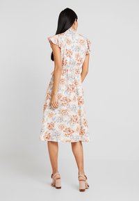 Blommig midiklänning med korta volangärmar, med en ljus bakgrund och orangea och blå blommor, cinchad midja och utsvängd nederdel.