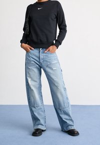 Black sweatshirt with white Nike logo, paired with light blue distressed wide-leg jeans and black chunky-soled boots. Textured fabric details visible.