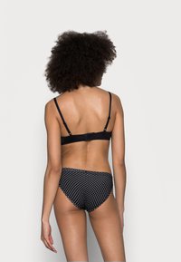 Bralette nera con spalline regolabili abbinata a slip neri a vita alta con pois. Tessuto liscio, design minimalista, dotato di chiusura a gancio.