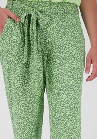 Pantaloni verzi cu imprimeu floral, dintr-un material ușor, având un brâu cu șnur și buzunare laterale, cu o textură subtilă și croială lejeră.