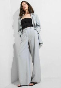 Ljust grå oversized blazer och vida byxor, parat med en svart strapless topp. Slät tyg med en subtil lyster, minimalistisk design.