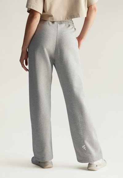 Sivé teplákové nohavice s voľným strihom, elastickým pásom a potlačeným logom na ľavej nohe. Materiál vyzerá jemne a štruktúrovaný.