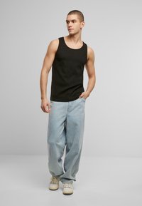 Black tank top with wide neckline, paired with light blue loose-fitting jeans and white sneakers, displayed on a model.