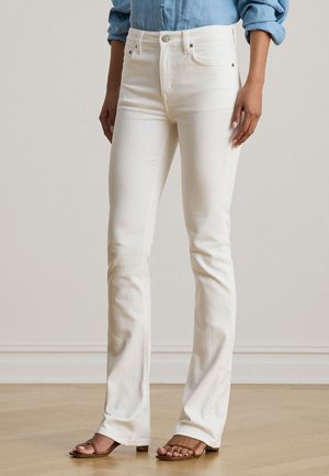 Άσπρο τζιν παντελόνι καμπάνα με ψηλή μέση, σχέδιο με πέντε τσέπες και διακριτικές ραφές. Ομαλή υφή, συνδυασμένο με καφέ επίπεδα σανδάλια.