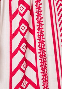 Bomullstyg med röda geometriska mönster, inklusive diamanter och linjer, på en vit bakgrund. Mjuk textur med tydliga, definierade accenter.