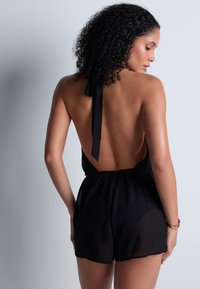 Romper noir à encolure halter, avec un dos nu, une taille élastique et une silhouette en tissu doux et transparent, doté d'une fermeture à nouer au cou.