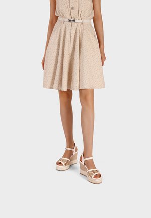 Donna che indossa un vestito beige a fantasia, lunghezza al ginocchio, con cintura e abbinato a sandali beige con zeppa platform intrecciata.