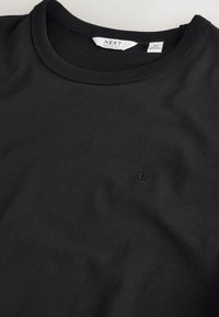 T-shirt noir à col rond avec petit logo couronne brodé sur la poitrine, taille indiquée médium, coupe régulière, fabriqué au Bangladesh.