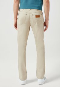 Beige rechtlopende broek van een gladde stof, met twee achterzakken en een leren logo patch. Gekocht met witte sneakers.