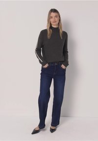 Tummanharmaa korkeakauluksinen neulepaita, jossa valkoiset raidat hihoissa, yhdistetty tummansinisiin suoralahkeisiin farkkuihin ja mustiin teräväkärkisiin tasapohjaisiin kenkiin.