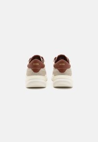 Paire de baskets BOSS beige et marron vues de dos avec des semelles blanches épaisses sur un fond clair uni.