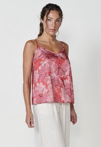 Camisole en satin rouge avec broderie florale, présentant des bretelles fines et une coupe décontractée. Associée à un pantalon en lin léger et fluide.