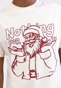 T-shirt branca de algodão com uma estampa vermelha do Pai Natal com barba, braços estendidos e o texto "Nada para ti" acima dele.
