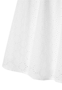 Vitt tyg med ett cirkulärt mönster, med broderade utskärningar som skapar en texturerad, spetsliknande look. Slät yta, lätt vikt.