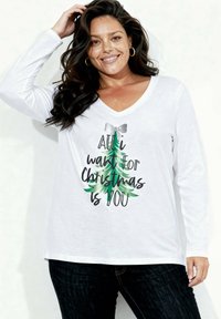 Biała koszulka z długim rękawem i dekoltem w serek, zdobiona zielonym nadrukiem choinki oraz czarnym napisem "All I want for Christmas is YOU." Miękka tkanina, luźny krój.