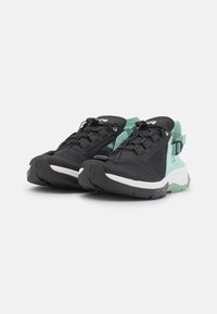 Zapatillas deportivas negras y verde azulado con paneles de malla, punta redondeada, suela texturizada, cordones y correa en el talón ajustable; logotipo de la marca visible.