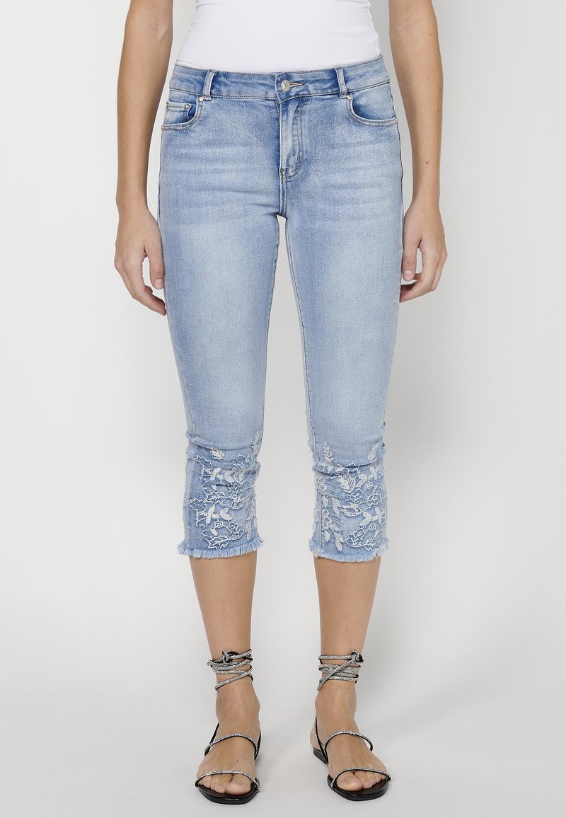 Svetlo modre denim capri hlače z uničenim robom, z cvetličnim vezenjem na manšettah, srednje visok pas in klasičen pet-pocket dizajn.