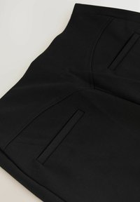 Černé látkové kalhoty s hladkým povrchem, dvěma předními kapsami a čistými švy. Design je jednoduchý a přizpůsobený pro obepnutý vzhled.