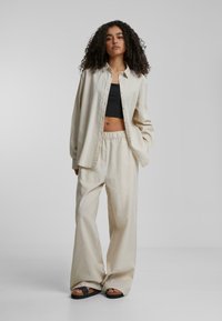 Lys beige oversized knappeskjorte, svart cropped topp og løstsittende bukser. Teksturert stoff, vide ben, kombinert med svarte sandaler.