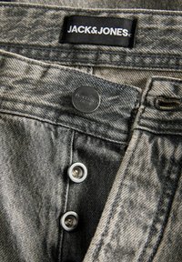 Sive jeans iz umetnosti z črno oznako "JACK & JONES." Vsebujejo kovinske gumbne zapore in kontrastne šive.