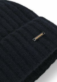Berretto lavorato a costine nero in lana morbida, con una piccola etichetta metallica accentuata in oro. Tessuto testurizzato per calore e comfort.