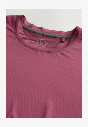 Tricou de activitate maron cu o suprafață texturată, guler rotund și banda gri la gulerul interior. Are o mică buclă pentru agățat.