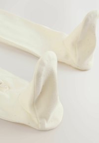 Bele bombažne nogavice z dolgočasnimi, okroglimi robovi, okrašenimi z majhnimi svetlimi pikami. Tkanina je videti mehka s subtilno teksturo.