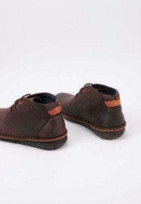 Scarpe alla caviglia in pelle marrone con un accento color pelle chiara sul tallone, caratterizzate da una punta arrotondata e cuciture in contrasto lungo la suola.
