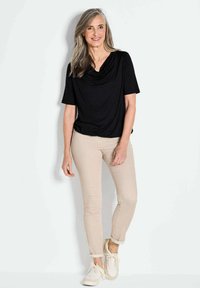 Schwarze Drapierte Oberteil, beigefarbene enganliegende Hose und weiße Sneakers. Glatter Stoff, lockere Passform, umgeschlagener Hosenbund und einfache Designdetails.