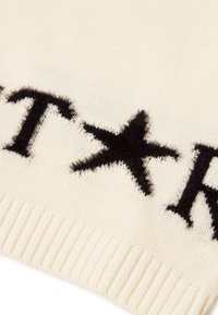 Sweter robiony na drutach w kolorze kremowym z czarnym napisem i wzorem gwiazdy. Posiada ściągacz na dole oraz miękką fakturę. Brak widocznych metek lub etykiet.