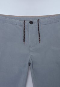Pantalones cortos grises con cierre de botón, cordón ajustable con acentos en negro y naranja, y una textura de tela suave.
