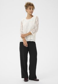 Hvid blondetop med trekvartærmer, scalloperet halsudskæring, parret med sorte brede bukser. Flade sko fuldender outfittet.