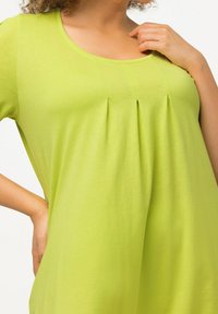 Limegrünes Oberteil aus weichem Stoff mit Rundhalsausschnitt und Faltendetails an der Brust, die eine lässige und lockere Passform schaffen.