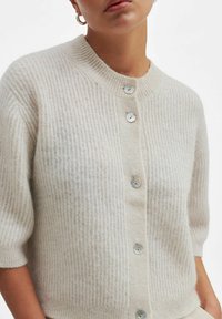 Lys beige cardigan laget av strukturert stoff, med ribbestruktur, korte ermer og rund hals med perle-lignende knapper.