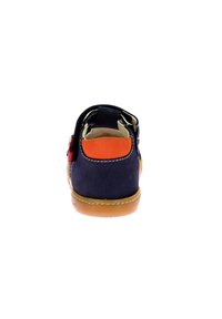 Navy suede children's shoe with a brown rubber sole, orange rear accent, and adjustable strap for secure fit. Smooth texture and streamlined shape.