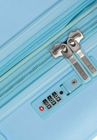 Valigia rigida di colore blu chiaro con doppie cerniere in metallo, lucchetto a combinazione e rifinitura testurizzata sulla cerniera e sul corpo.