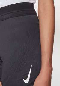 Zwarte sportshorts van een gestructureerde, ribbelige stof met een brede elastische tailleband, voorzien van een opvallend wit Nike-logo aan de zijkant.